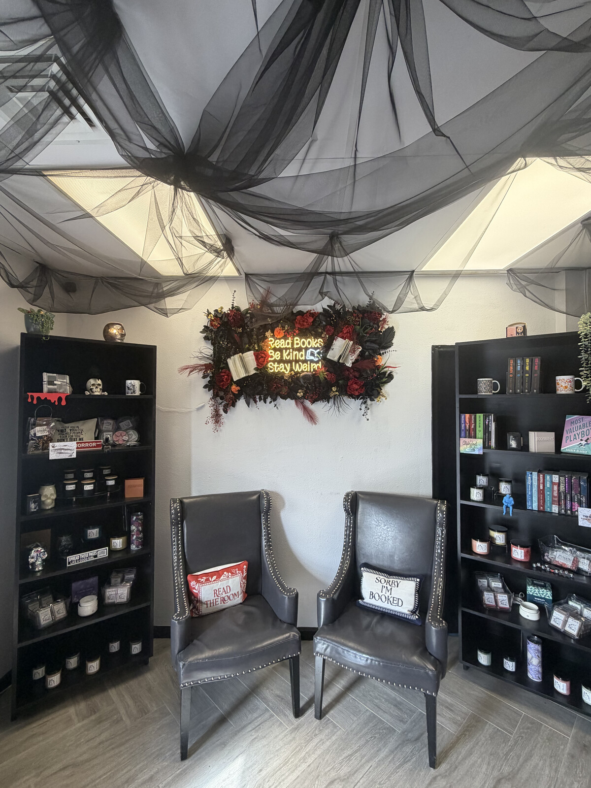 Inside The Damned Boutique — black tulle draped ceiling, twin gothic chairs, Til Death candles, and a 'Read Books · Be Kind · Stay Weird' neon
